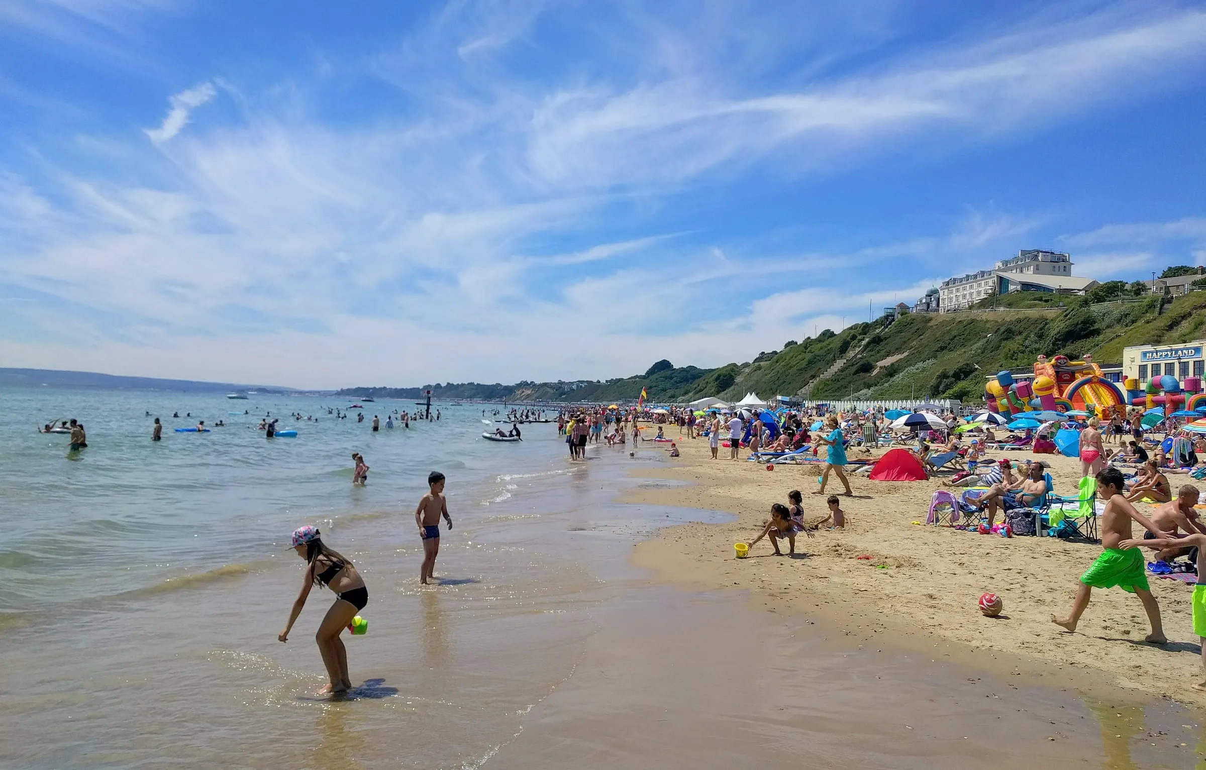 La playa de Bournemouth llena de gente un día de verano, con los acantilados al fondo.