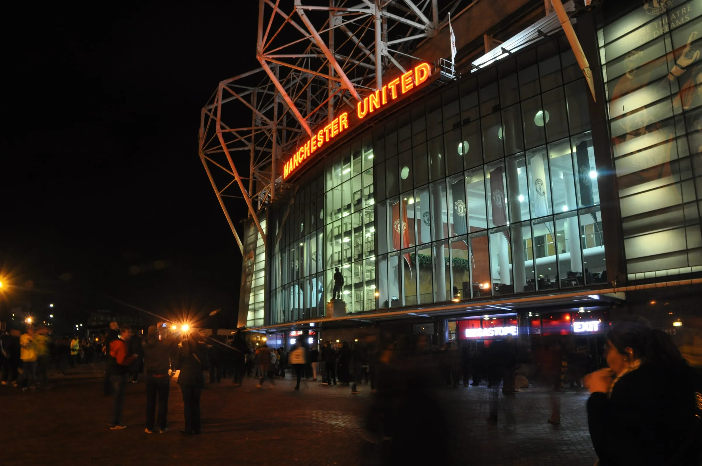 La fachada de Old Trafford de noche, con el letrero de Manchester United iluminado