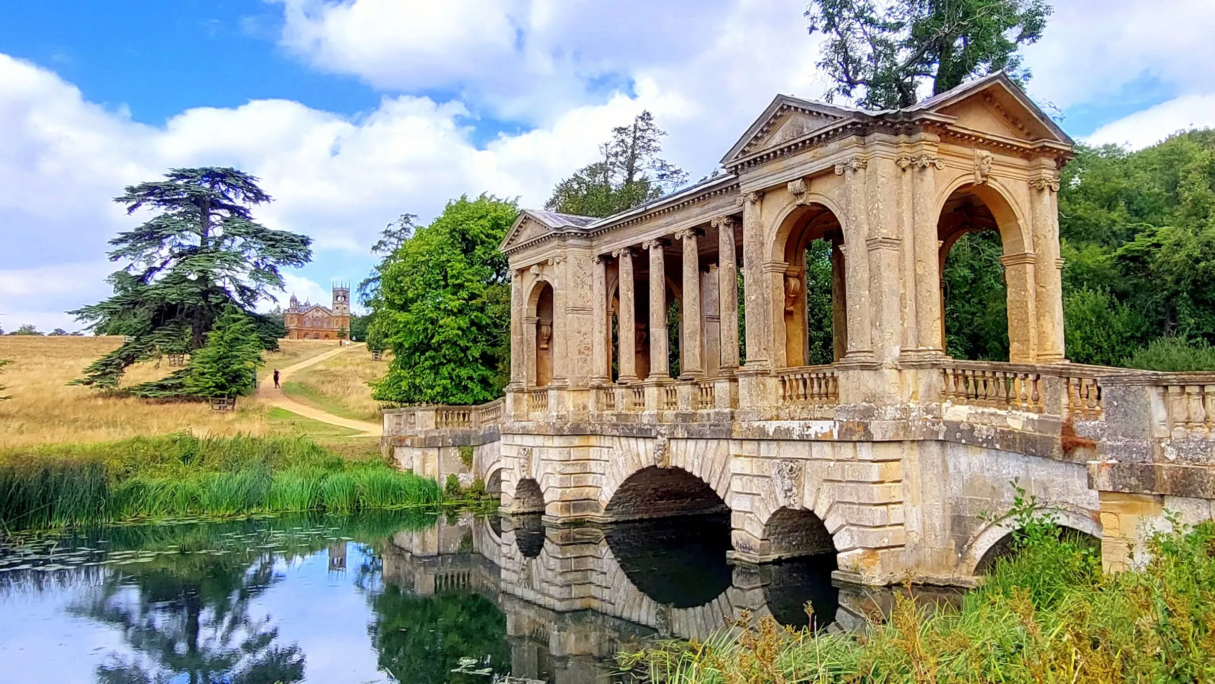 Puente palladiano de piedra sobre un lago entre árboles, en los jardines del colegio