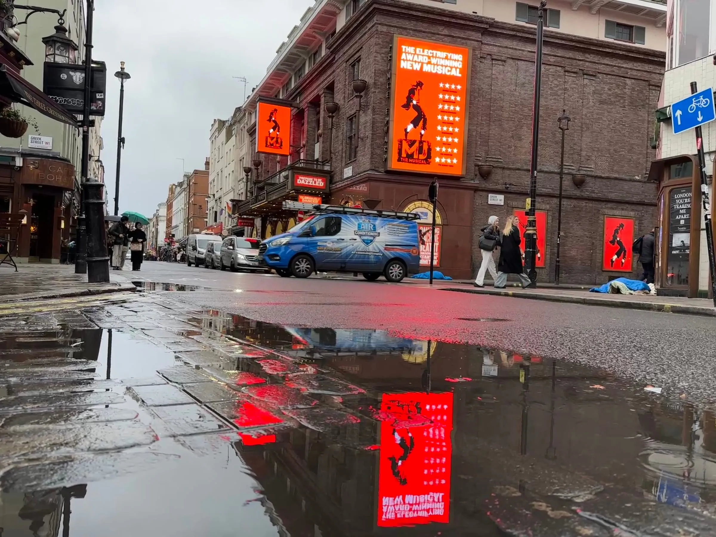 Los carteles de un musical reflejados en la calle mojada de Soho